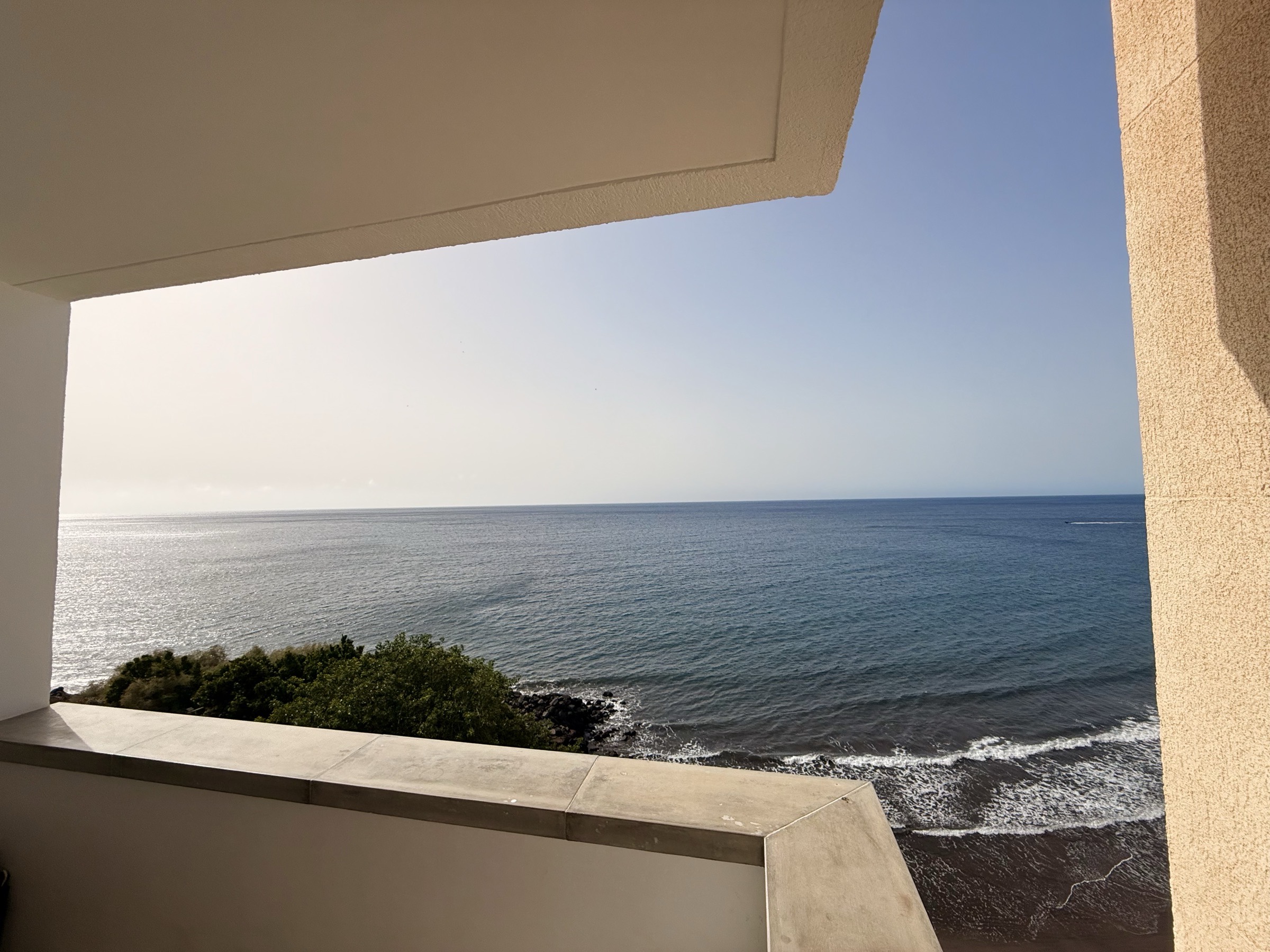 The sea framed by the concrete of the terrace — rocks, dark sand and open Atlantic below
